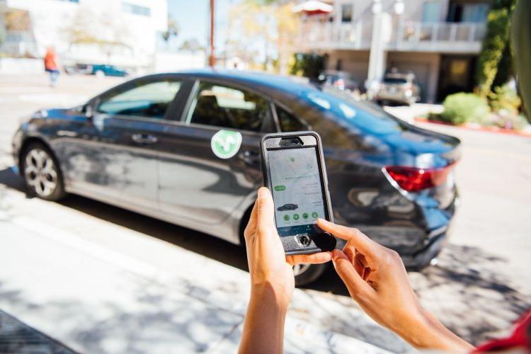a person holds a phone to look at an app in front of a rentable car